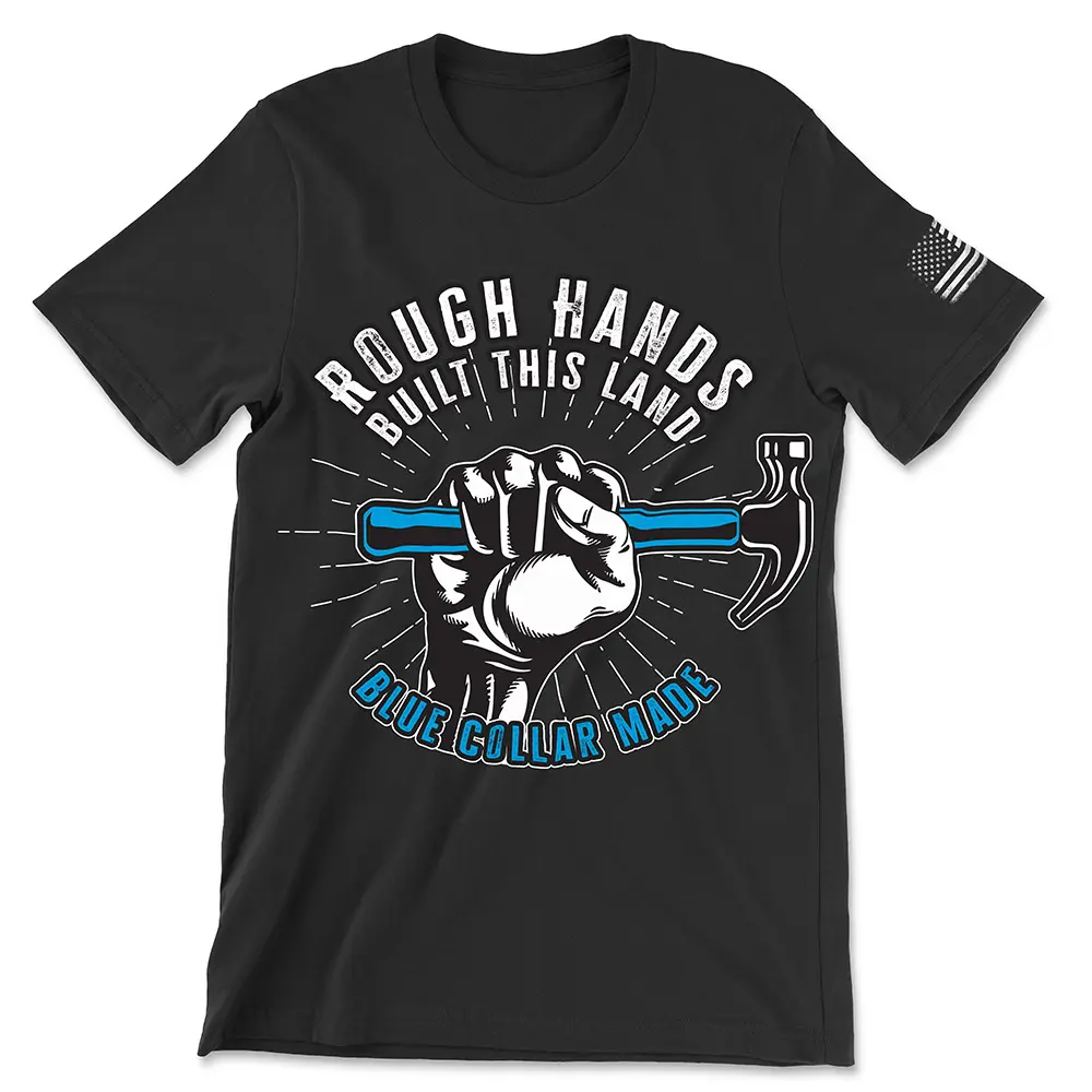 Black t-shirt with white text in circular shape "Rough hands" with "Built this land" directly below it at the top of the circle with "Blue collar made" in blue text with black and white outline at the bottom of the circle. A white and black fist gripping a hammer with a blue handle emerges from the bottom text into the center of the circle shape. White lines come from all around the fist moving toward the outside of the circle. Features white worn American flag on left sleeve.